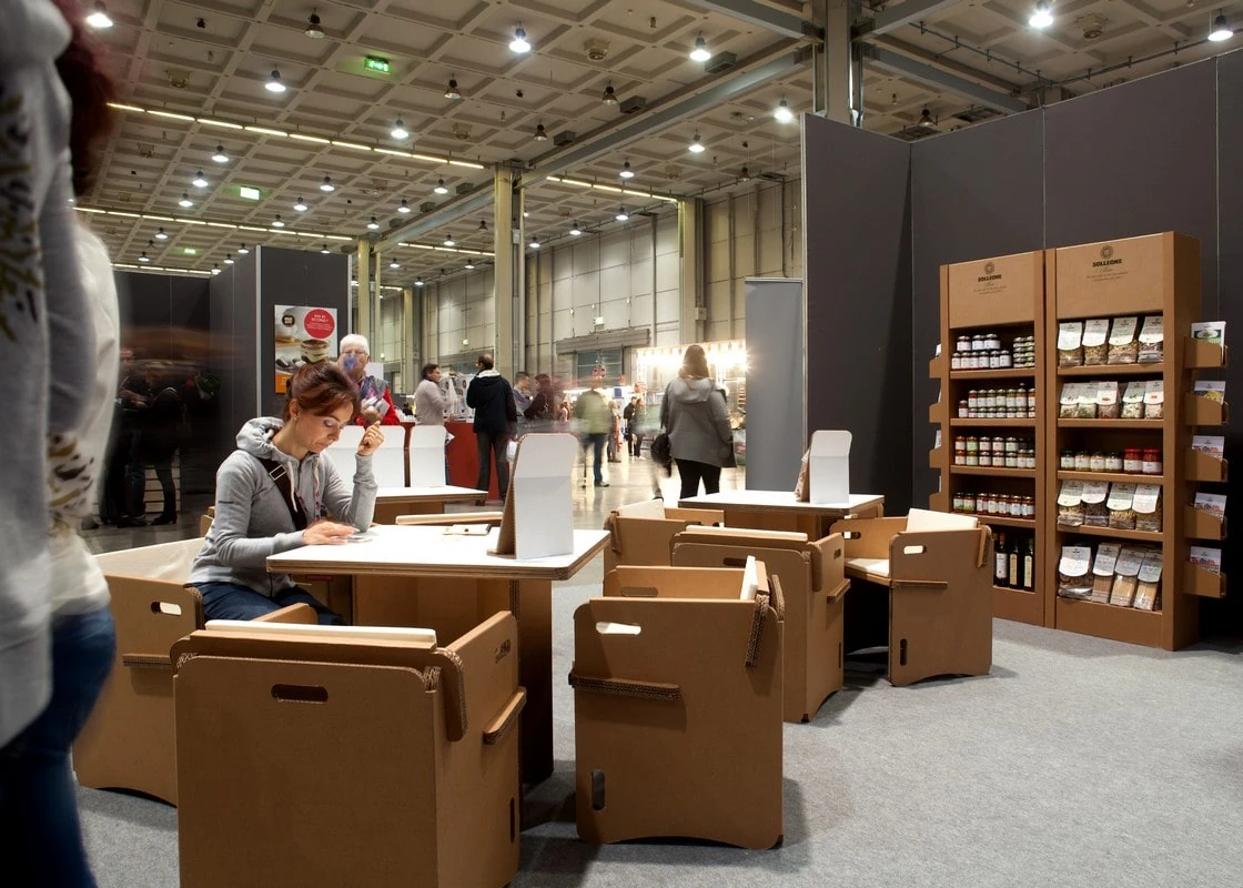 Odpočinková zóna s lepenkovými stolky a křesly a regály s produkty